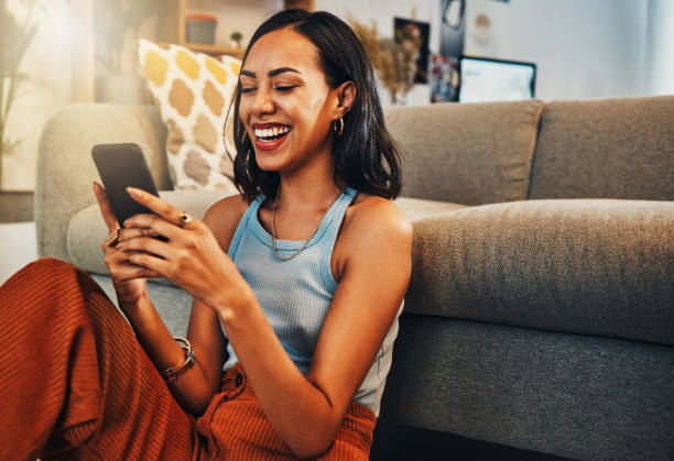 Beautiful mixed race woman browsing internet on cellphone in home living room. Happy hispanic sitting alone on floor in lounge and using technology to network. Laughing while scrolling on social media Beautiful mixed race woman browsing internet on cellphone in home living room. Happy hispanic sitting alone on floor in lounge and using technology to network. Laughing while scrolling on social media someone happy on their phone stock pictures, royalty-free photos & images